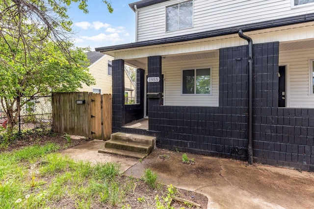 property entrance featuring fence, covered porch, and a gate