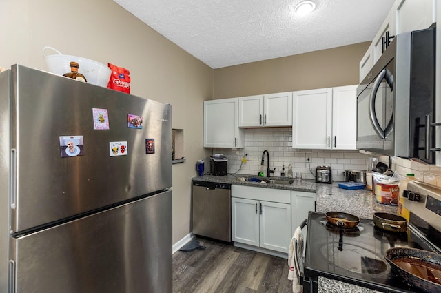 kitchen featuring a textured ceiling, a sink, appliances with stainless steel finishes, dark wood-style flooring, and light stone countertops