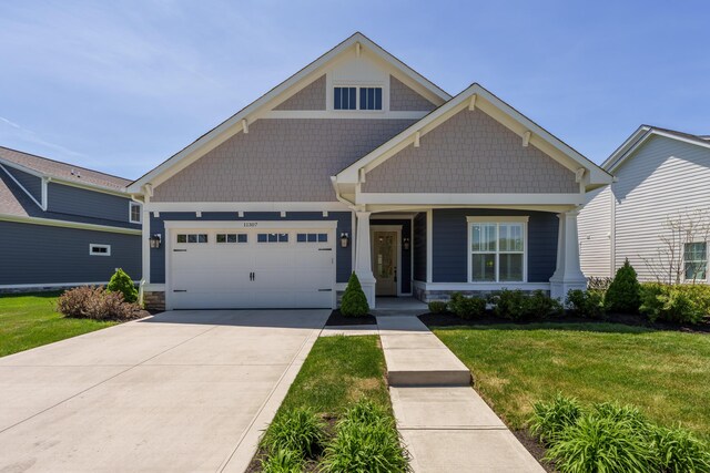 craftsman house with covered porch, a garage, a front lawn, concrete driveway, and stone siding