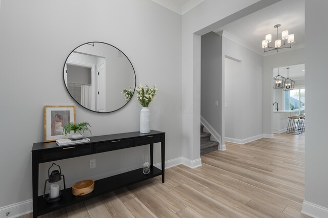 entryway featuring crown molding, baseboards, a notable chandelier, and light wood-style flooring