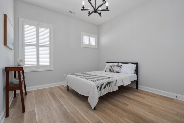 bedroom featuring an inviting chandelier, baseboards, light wood-style flooring, and visible vents