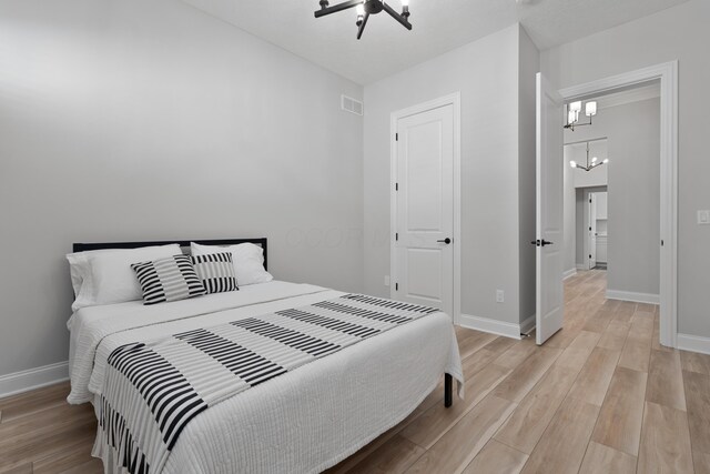 bedroom featuring baseboards, a notable chandelier, light wood finished floors, and visible vents