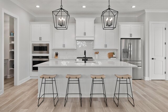 kitchen with a sink, appliances with stainless steel finishes, a kitchen island with sink, and a notable chandelier