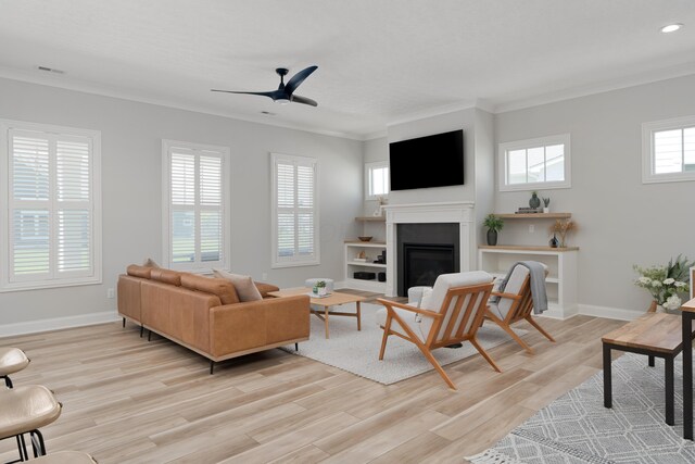living room featuring ceiling fan, visible vents, light wood finished floors, a glass covered fireplace, and ornamental molding