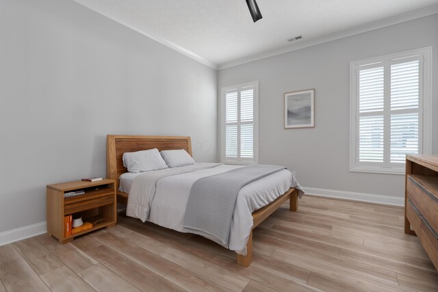 bedroom featuring crown molding, visible vents, baseboards, a ceiling fan, and light wood finished floors