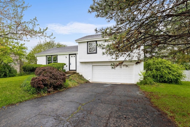 tri-level home featuring asphalt driveway, an attached garage, a front lawn, brick siding, and roof with shingles