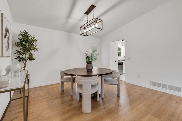 dining space featuring light wood-style floors, lofted ceiling, baseboards, and a chandelier