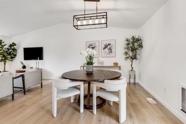 dining room featuring vaulted ceiling, light wood-style floors, and baseboards
