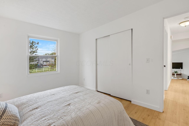 bedroom with light wood finished floors, a closet, and baseboards