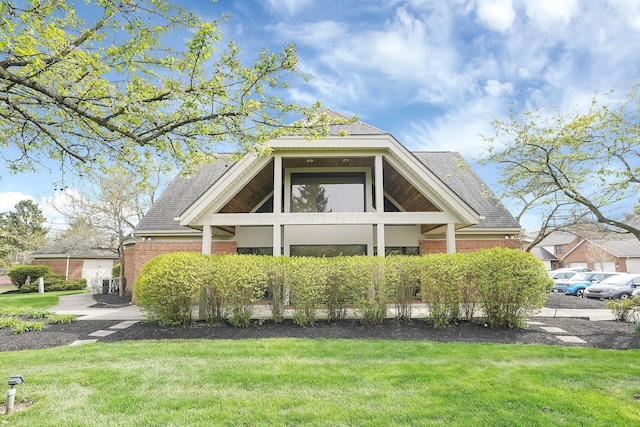 view of front of property with a front lawn, brick siding, and roof with shingles
