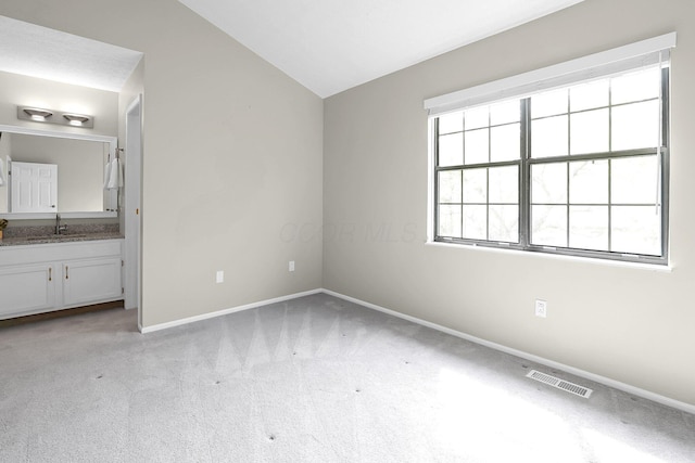 unfurnished bedroom featuring vaulted ceiling, visible vents, light carpet, a sink, and baseboards