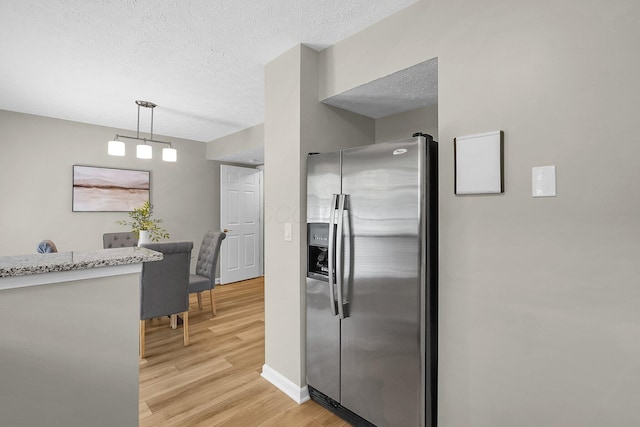 kitchen featuring stainless steel fridge with ice dispenser, decorative light fixtures, light wood-type flooring, baseboards, and a textured ceiling