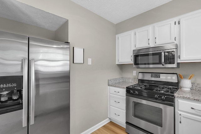 kitchen with light stone counters, a textured ceiling, light wood-type flooring, stainless steel appliances, and white cabinetry