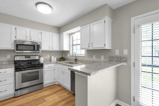 kitchen with white cabinets, stainless steel appliances, a sink, light wood-type flooring, and light stone counters
