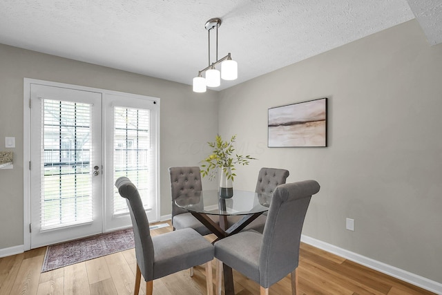 dining room featuring light wood-type flooring, a textured ceiling, and baseboards