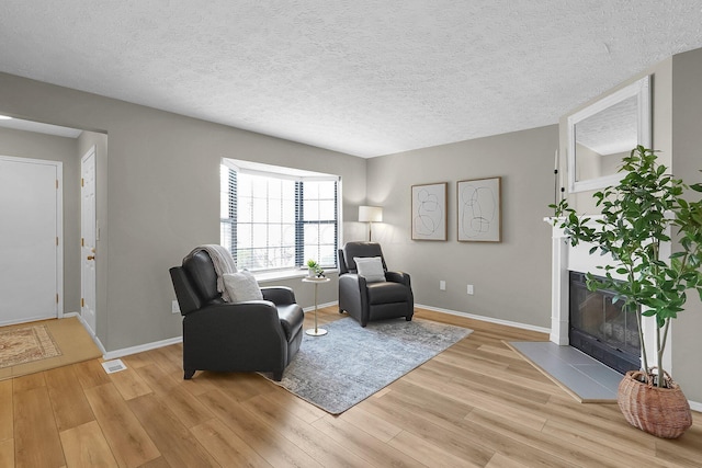 living area featuring a textured ceiling, baseboards, visible vents, light wood-style floors, and a tile fireplace