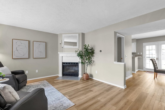 living room featuring baseboards, a glass covered fireplace, a textured ceiling, and light wood-type flooring