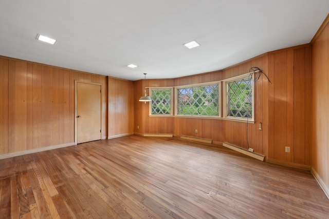 spare room featuring light wood-type flooring, a baseboard radiator, and wooden walls