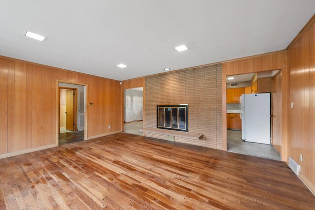unfurnished living room with a brick fireplace, wood walls, visible vents, and light wood-type flooring