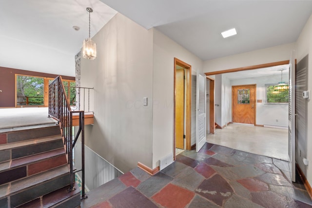 staircase featuring an inviting chandelier, baseboards, and stone tile floors