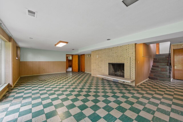 finished below grade area with visible vents, wood walls, stairs, a brick fireplace, and baseboards