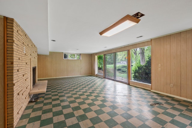 unfurnished living room featuring wooden walls, baseboards, a brick fireplace, and visible vents