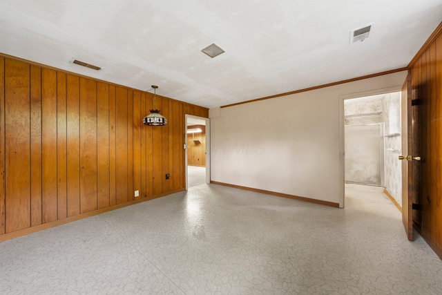 spare room featuring wooden walls, baseboards, visible vents, and crown molding
