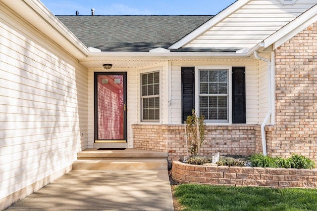 view of exterior entry with brick siding and a shingled roof
