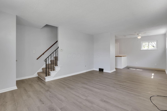unfurnished living room featuring ceiling fan, stairs, baseboards, a textured ceiling, and wood finished floors