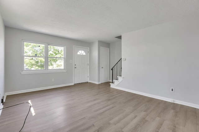 foyer featuring a textured ceiling, wood finished floors, stairs, and baseboards