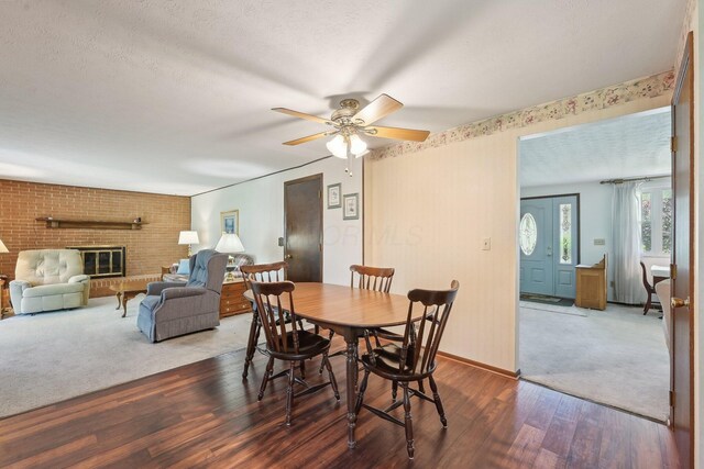 dining area featuring wood finished floors, carpet flooring, a brick fireplace, baseboards, and a ceiling fan