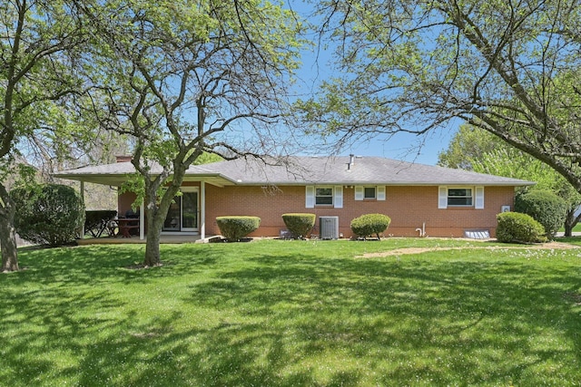 rear view of property with a lawn, a chimney, central AC, and brick siding