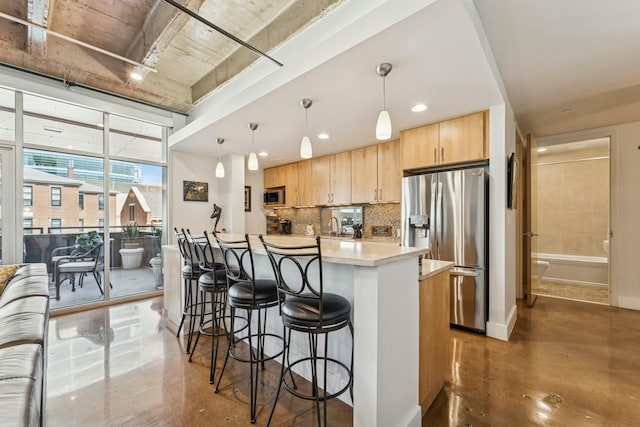 kitchen featuring tasteful backsplash, light brown cabinets, appliances with stainless steel finishes, finished concrete flooring, and a kitchen breakfast bar