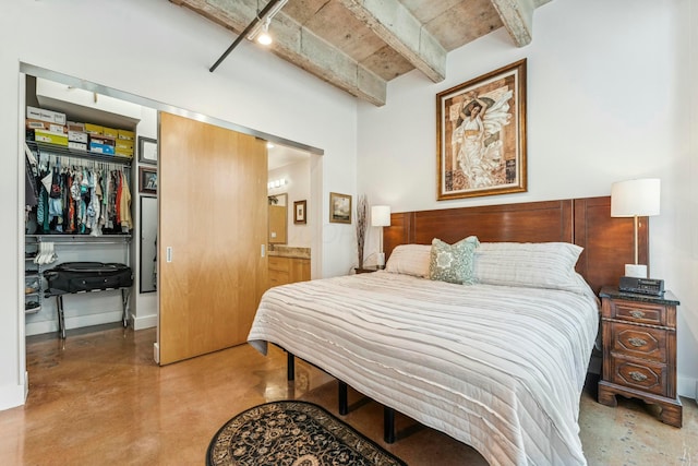 bedroom with a closet, ensuite bath, track lighting, a walk in closet, and finished concrete floors