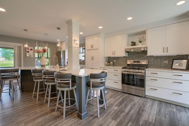 kitchen with under cabinet range hood, decorative backsplash, dark wood-type flooring, light countertops, and appliances with stainless steel finishes