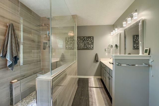 bathroom featuring a tile shower, a textured ceiling, vanity, and baseboards