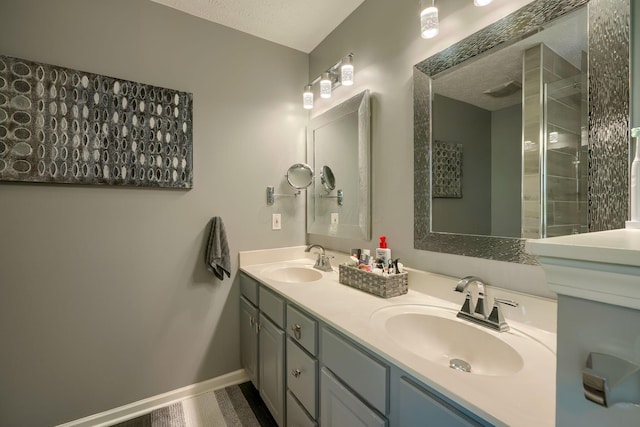 bathroom with a tile shower, double vanity, a sink, and a textured ceiling