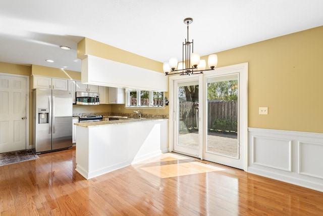 kitchen featuring appliances with stainless steel finishes, plenty of natural light, light wood-style flooring, a chandelier, and a wainscoted wall