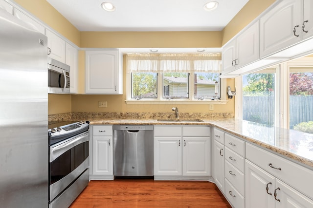 kitchen featuring appliances with stainless steel finishes, a sink, recessed lighting, white cabinetry, and light stone counters