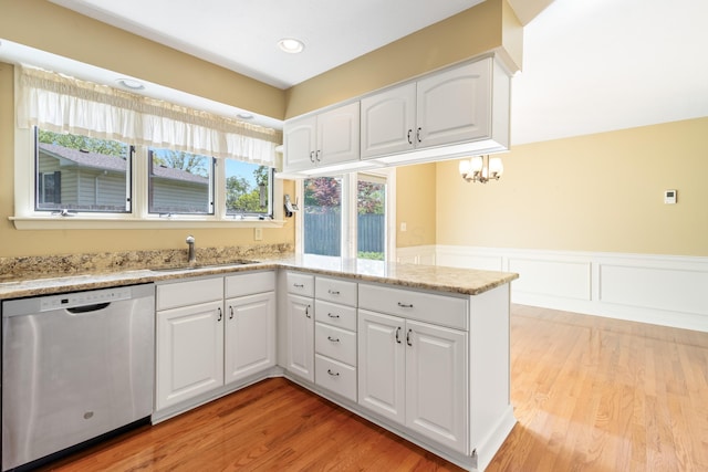 kitchen featuring stainless steel dishwasher, a sink, light wood-style flooring, a peninsula, and a wainscoted wall