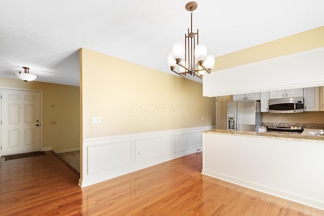 kitchen with stainless steel appliances, a chandelier, light wood-style floors, decorative light fixtures, and a wainscoted wall