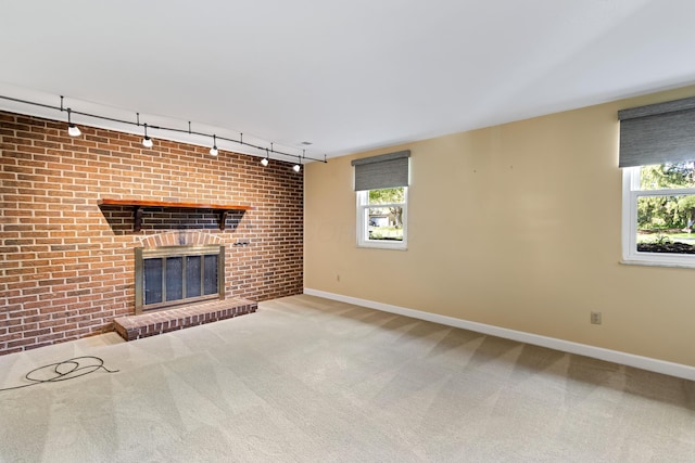 unfurnished living room with track lighting, carpet flooring, a brick fireplace, and baseboards