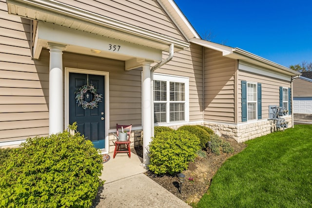 view of exterior entry with a lawn, stone siding, and covered porch