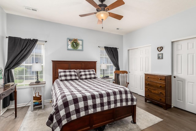 bedroom featuring multiple closets, wood finished floors, visible vents, and ceiling fan
