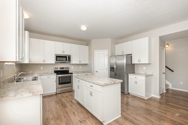 kitchen with a kitchen island, appliances with stainless steel finishes, a sink, light countertops, and light wood-style floors