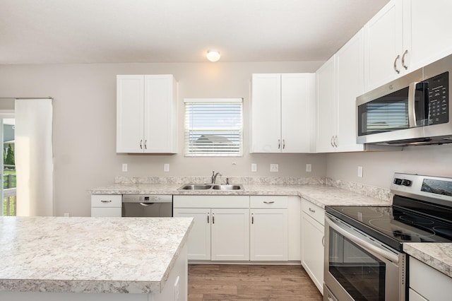 kitchen with appliances with stainless steel finishes, a sink, light wood finished floors, light countertops, and white cabinetry