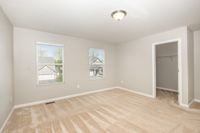 unfurnished bedroom featuring visible vents, a closet, light carpet, baseboards, and a walk in closet
