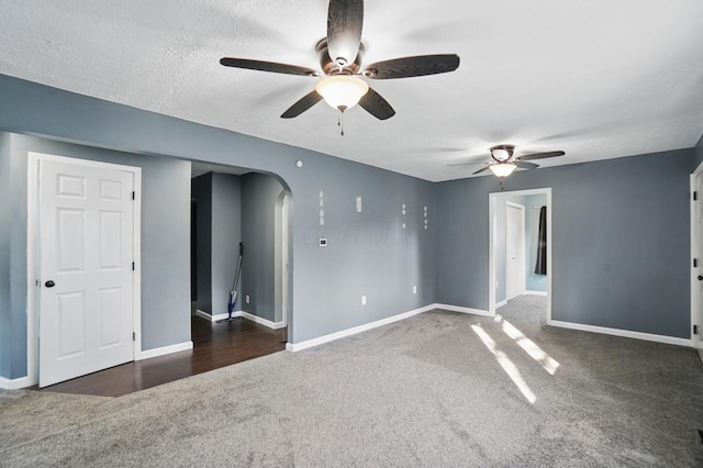 empty room with arched walkways, a ceiling fan, carpet flooring, and baseboards