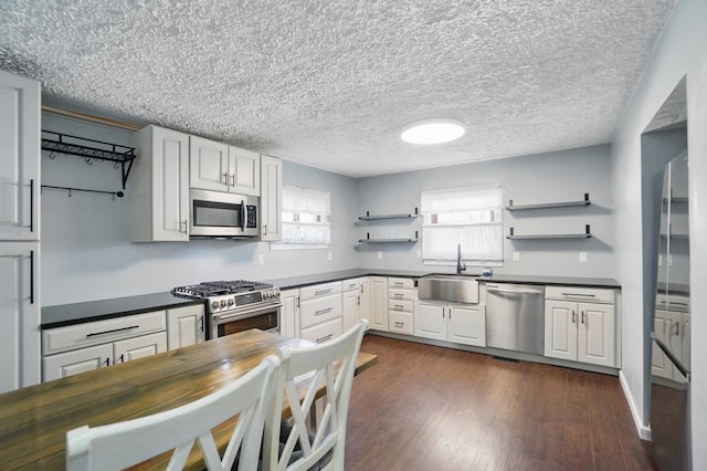 kitchen with dark countertops, appliances with stainless steel finishes, open shelves, and a sink