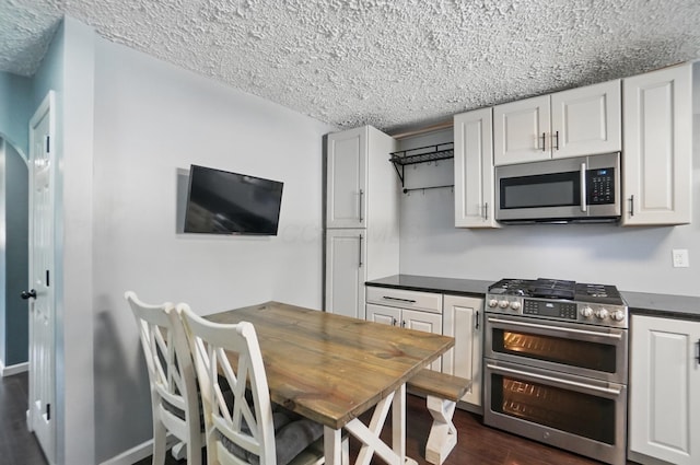 kitchen with dark countertops, a textured ceiling, stainless steel appliances, dark wood finished floors, and white cabinetry
